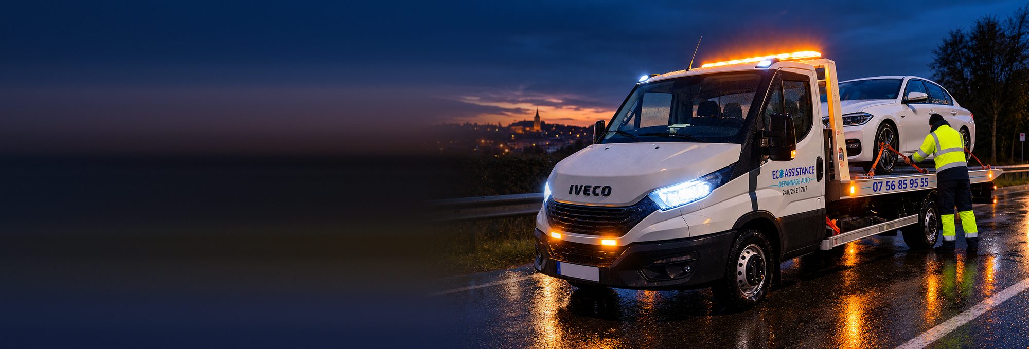 Dépanneuse plateau Iveco Daily ECO ASSISTANCE chargeant une voiture au bord de la route, à la tombée de la nuit, près de Villefranche-sur-Saône